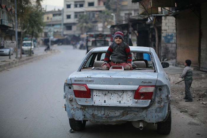 Un niño sentado sobre un coche destrozado por una explosión en Guta (Siria). Foto: Save the Children.