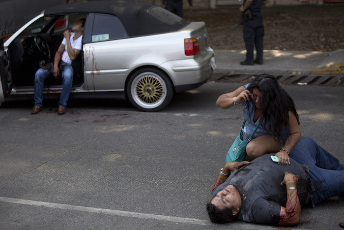 En esta foto del 13 de mayo de 2016, una mujer conversa por teléfono frente a una persona herida, Edgar Osvaldo Vega, mientras Pedro Gracias permanece herido y sentado en un vehículo en espera de ayuda después de que los balearan mientras viajaban en un vehículo cerca de la playa de Caleta en Acapulco, México. La policía llegó pero no alguna ambulancia que llevara a los heridos a un hospital. Foto: AP