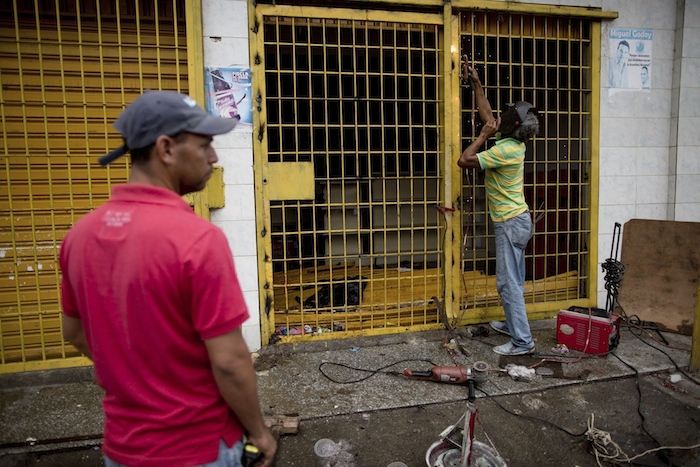 El dueño de un supermercado repara la puerta de seguridad del comercio saqueado por manifestantes en Ciudad Bolívar, Venezuela, el lunes 19 de diciembre de 2016. foot: AP.