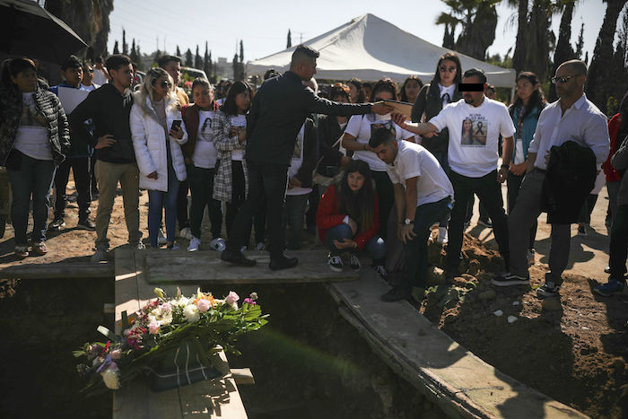 Un hombre llamado Juan, segundo por la derecha, que fue detenido en relación con la desaparición y el asesinato de Marbella Valdez, entrega un retrato de la víctima al ex novio de Valdez, Jairo Solano, junto a la hermana de la víctima, Brenda, arrodillada, y su padrastro, William H. Hessik, en el extremo a la derecha, durante el entierro en un cementerio de Tijuana, México, el viernes 14 de febrero de 2020. Foto: Emilio Espejel, AP