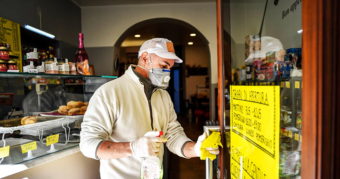 Un hombre desinfecta la puerta de un negocio de Codogno, epicentro del brote de coronavirus en Italia, el 11 de marzo del 2020. Foto: Claudio Furlan, LaPresse vía AP