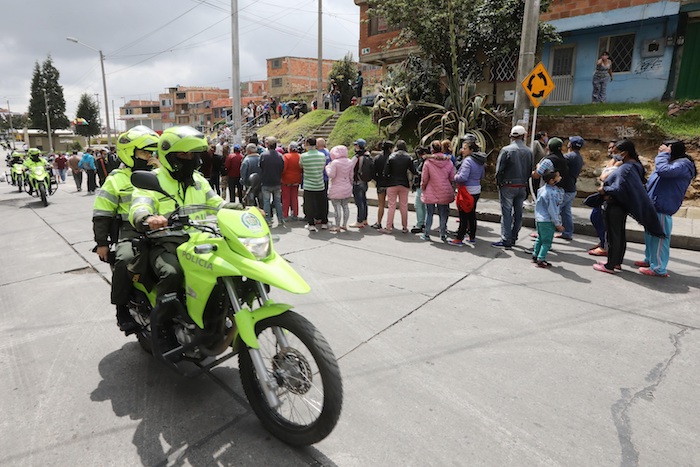 Un grupo de policías fue registrado este martes al patrullar las calles de Ciudad Bolívar, uno de los sectores más pobres de Bogotá (Colombia), mientras personas hacen fila para inscribirse a las ayudas alimentarias del Gobierno durante la cuarentena por el COVID-19. 