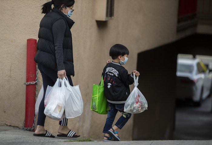 En esta fotografía del 2 de abril de 2020, un adulto y un niño que portan mascarillas cargan unas bolsas en Los Ángeles, durante la pandemia del nuevo coronavirus.