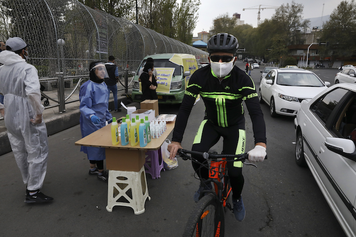 Un ciclista con mascarilla para combatir el contagio de coronavirus pasa junto a varias personas vendiendo desinfectante de manos a bajo precio en la plaza Tajrish, en el norte de Teherán, Irán, el jueves 16 de abril de 2020.