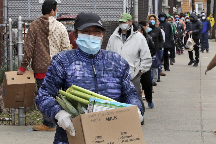 Una mujer se lleva una caja con comida mientras cientos de personas siguen haciendo cola en un centro de asistencia a los necesitados en Chelsea, Massachusetts, el 22 de abril del 2020. Chelsa es un suburbio de Boston mayormente hispano con la concentración de casos de coronavirus más grande de Massachusetts.