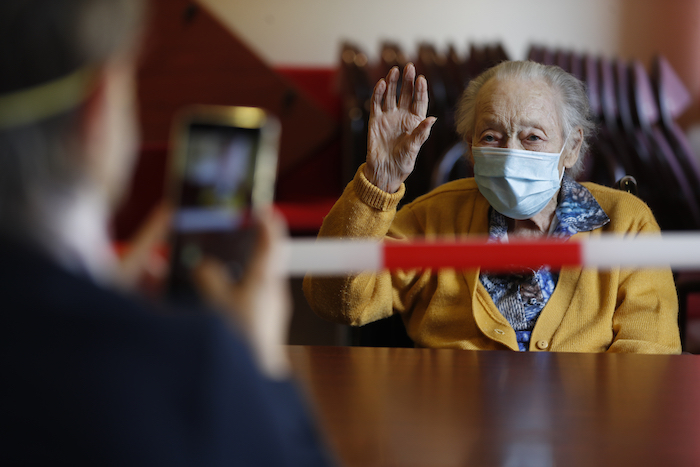 Margarite Mouille, de 94 años, gesticula mientras su hija le toma una foto en una residencia para ancianos de Kaysersberg, Francia, el 21 de abril del 2020. Francia volvió a permitir esas visitas, aunque muy reguladas, siempre con una mesa y una cinta roja y blanca de por medio.