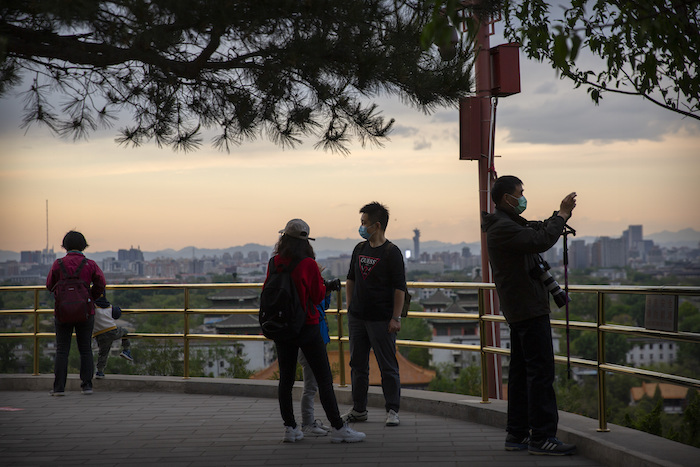 Varias personas con máscaras para protegerse del nuevo coronavirus observan el panorama desde lo alto de una colina en un parque público en Beijing, el sábado 25 de abril de 2020.