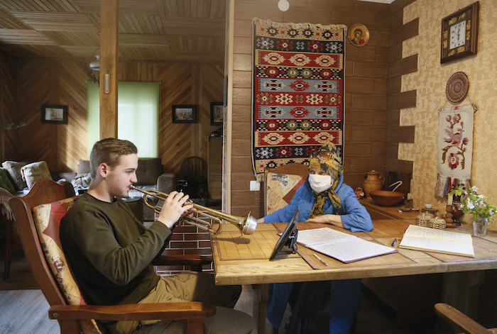 Un estudiante practica la trompeta durante una clase por internet para preparar su examen final en una escuela de música, junto a su abuela, protegida por una mascarilla, en el pueblo de Stari Petrivtsi, cerca de la capital de Ucrania, Kiev, a las 18:00 del viernes 24 de abril de 2020. 