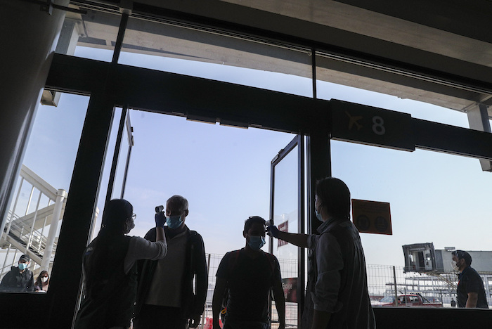 Trabajadores de la salud le miden la temperatura a los chilenos después de aterrizar en el aeropuerto Arturo Merino Benítez en Santiago, Chile, el viernes 8 de mayo de 2020. 