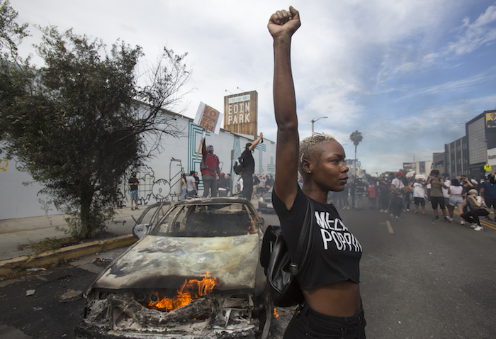 Una manifestante posa para la prensa ante un vehículo policial en llamas en Los Ángeles, el sábado 30 de mayo de 2020, durante una manifestación por la muerte de George Floyd, un hombre afroamericano que murió tras ser detenido por la policía en Minneapolis, el 25 de mayo de 2020. 