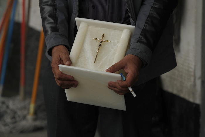 Con un cigarrillo en la mano, un hombre sostiene una urna para cenizas humanas mientras observa el cuerpo de un familiar, que murió de COVID-19, mientras trabajadores lo llevan al interior del crematorio en el Panteón San Nicolás Tolentino en la Alcaldía Iztapalapa, Ciudad de México, el martes 2 de junio de 2020.