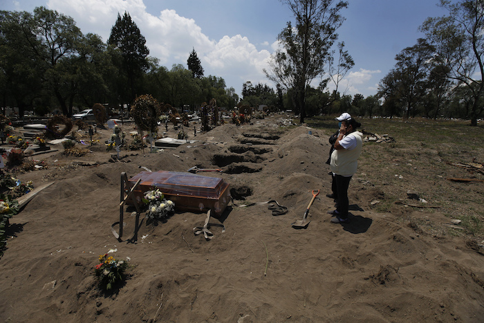 Personas ven el ataúd de un familiar que murió de COVID-19 antes de descender a una tumba en el Panteón de San Lorenzo Tezonco Iztapalapa en una sección reservada para víctimas del nuevo coronavirus en la Alcaldía Iztapalapa en Ciudad de México, el martes 2 de junio de 2020. Bajo una norma especial para contener la propagación de la pandemia, sólo se permite que dos familiares acompañen al ataúd a la tumba. 