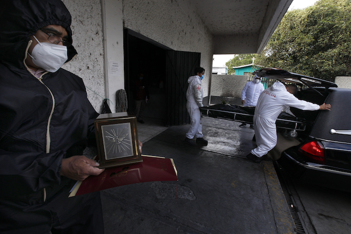 Un hombre que sostiene una urna observa el cadáver de un familiar que murió de COVID-19 mientras empleados lo llevan al crematorio del Panteón San Nicolás Tolentino en la Alcaldía Iztapalapa en Ciudad de México el martes 2 de junio de 2020. 