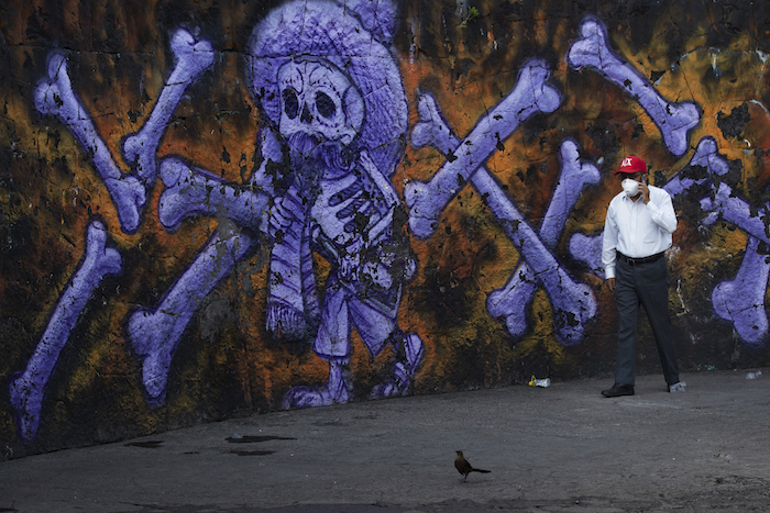 Arturo Morales Torres, responsable de varios cementerios públicos, habla en su celular frente a un mural de un esqueleto y huesos que decora el exterior del Panteón San Nicolás Tolentino en la Alcaldía Iztapalapa en Ciudad de México el jueves 4 de junio de 2020 durante la pandemia del nuevo coronavirus. 