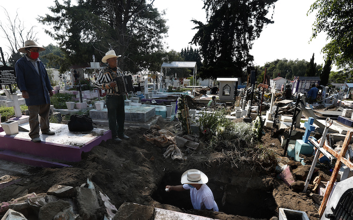 El músico de cementerio Víctor Dzib Cima, de 70 años, toca su acordeón mientras espera clientes cuando trabajadores de cementerio retiran ataúdes de tumbas que pertenecen a familiares que dejaron de pagar alquiler en el cementerio San Nicolás Tolentino, en donde ha trabajado a cambio de propinas durante 22 años en la Alcaldía Iztapalapa en Ciudad de México el viernes 22 de mayo de 2020. 