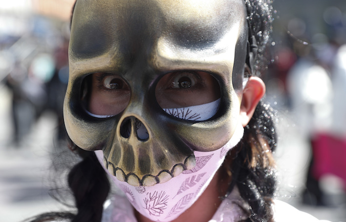 Un artista usando una mascarilla contra la pandemia del coronavirus bajo una máscara de calavera marcha para protestar contra el Gobierno en La Paz, Bolivia, el lunes 8 de junio de 2020. 