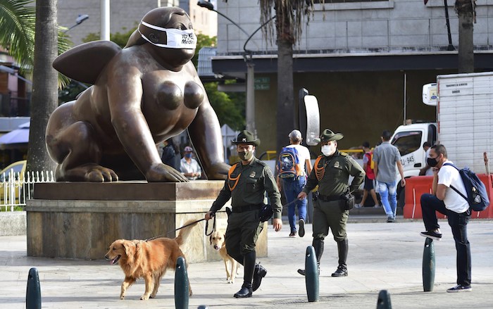 Policías con máscaras faciales patrullan cerca de la escultura del artista colombiano Fernando Botero con una mascarilla durante una campaña sobre el nuevo coronavirus en Medellín, Colombia, el 9 de junio de 2020. 