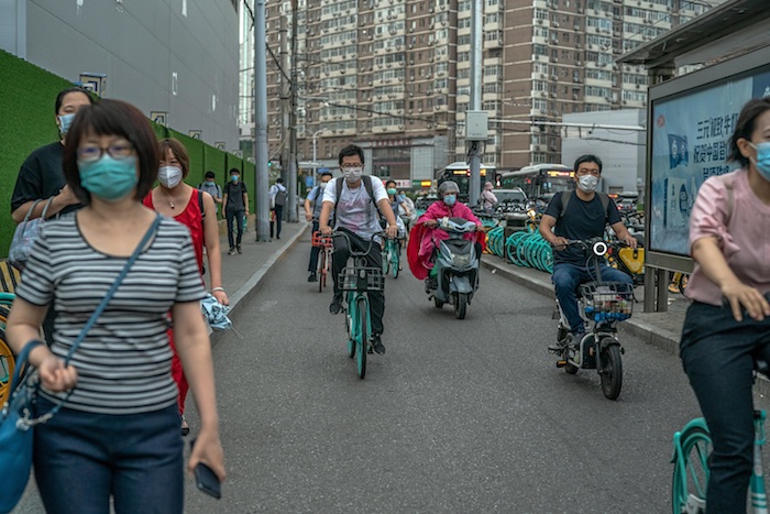 Gente cubierta con mascarillas camina por las calles entre bicicletas y scooters, en Pekín. 