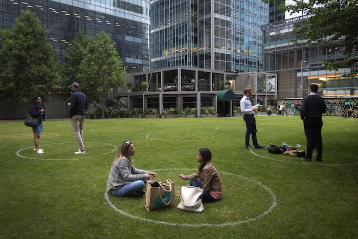 Esta fotografía del miércoles 1 de julio de 2020 muestra a clientes de un bar sentados en círculos trazados sobre el césped para guardar la distancia social, en Canary Wharf, en el este de Londres, al levantarse gradualmente las restricciones relacionadas con el coronavirus en Inglaterra.