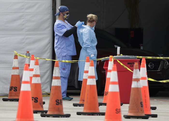 Trabajadores de la salud se ayudan mutuamente a colocarse equipo protector en un sitio de testeo del coronavirus en Miami Gardens, Florida, 5 de julio de 2020. El equipo protector para los trabajadores que atienden a enfermos de COVID-19 vuelve a escasear.