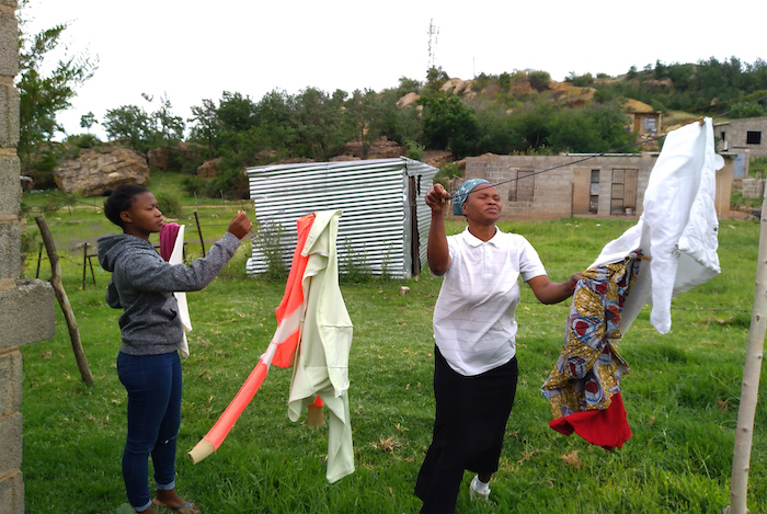 Matefo Litali (der) y su hija Refiloe recogen ropa que se secó al sol en su casa de Ha Thetsane, en Maseru, Lesotho, el 12 de diciembre del 2020. Litali fue despedida por la fábrica textil donde trabajaba ante la escasez de pedidos por la pandemia del coronavirus. 