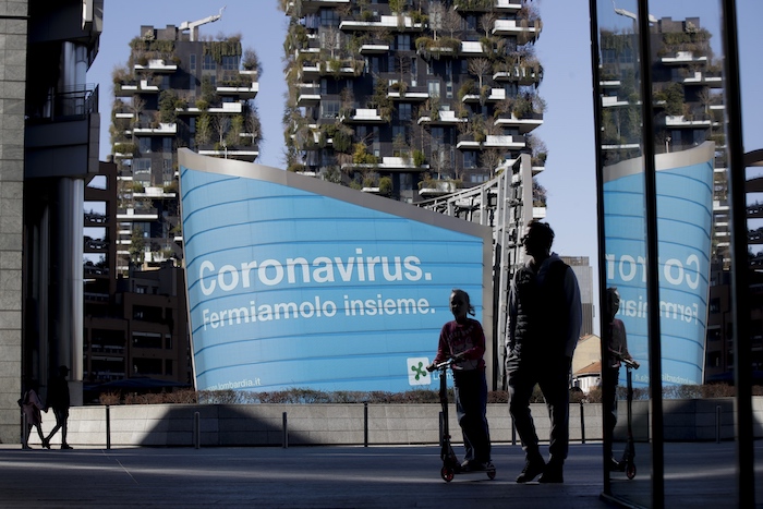 En esta imagen de archivo, tomada el 11 de marzo de 2020, un hombre y una niña en un patinete caminan pasan por delante de una pantalla donde se emite una campaña publicitaria de la región de Lombardía con el lema (en italiano) "Coronavirus, parémoslo juntos", en el distrito de Porta Nuova, en Milán. En ese día, Italia cerró tiendas y restaurantes luego de aislarse tras alcanzar los 10 mil contagios.