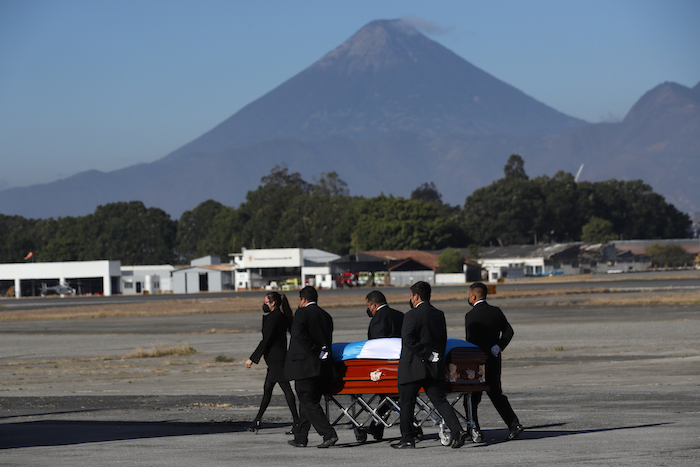 Personas transportan un ataúd cubierto con banderas en la pista mientras los restos de 16 migrantes guatemaltecos que murieron cerca de la frontera entre Estados Unidos y México en enero llegan a la base de la Fuerza Aérea en la Ciudad de Guatemala, el viernes 12 de marzo de 2021. 