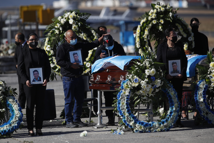 Personas de pie esperan con fotografías mientras las familias reciben los restos de 16 migrantes guatemaltecos que fueron asesinados cerca de la frontera entre Estados Unidos y México en enero que llegaron a la base de la Fuerza Aérea en Ciudad de Guatemala, el viernes 12 de marzo de 2021.