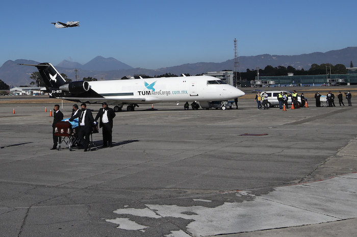 Personas transportan ataúdes cubiertos con banderas en la pista mientras los restos de 16 migrantes guatemaltecos que murieron cerca de la frontera entre Estados Unidos y México en enero llegan a la base de la Fuerza Aérea en la Ciudad de Guatemala, el viernes 12 de marzo de 2021. 