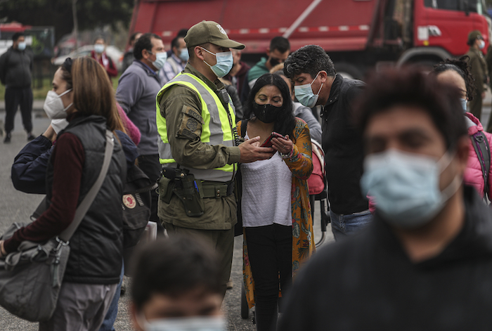 Un oficial de policía verifica los permisos de tránsito de las personas el jueves 1 de abril de 2021 en medio de una cuarentena por la pandemia de coronavirus afuera del Mercado Central, donde los compradores aguardan a comprar pescado para la Semana Santa, en Santiago, Chile. 