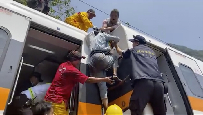 En esta imagen tomada de un video publicado por hsnews.com.tw, un pasajero (centro) recibe ayuda para subir encima de un tren descarrilado en la región de Hualien, en el este de Taiwán, el 2 de abril de 2021.