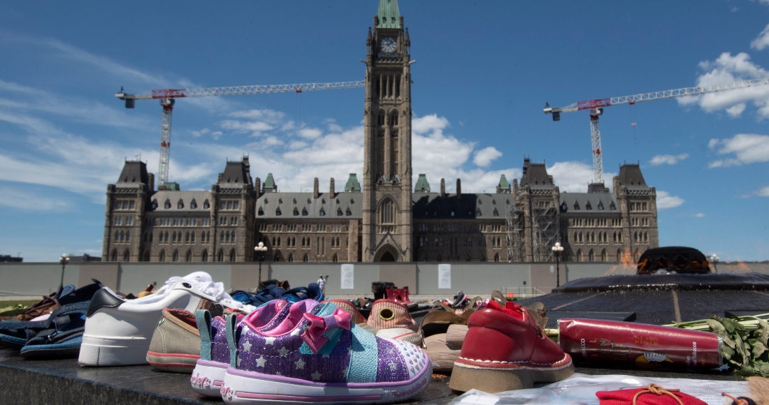 Zapatos, letreros y tabaco son colocados frente al Parlamento, en Ottawa, Ontario, el lunes 31 de mayo de 2021, en reconocimiento al descubrimiento de los cadáveres de decenas de niños en el sitio de un antiguo internado en Kamloops, Columbia Británica.