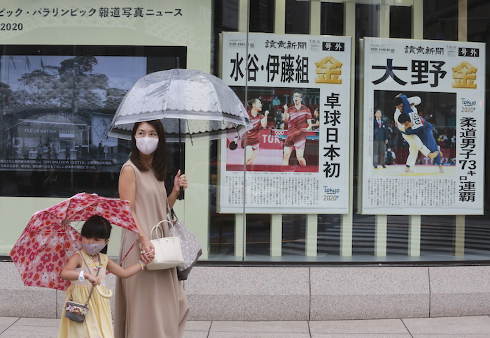 Dos personas, con mascarilla para protegerse del coronavirus, pasan por delante de una ventana con ediciones especiales de diarios con los oros olímpicos de Japón, en Tokio, el 27 de julio de 2021. 