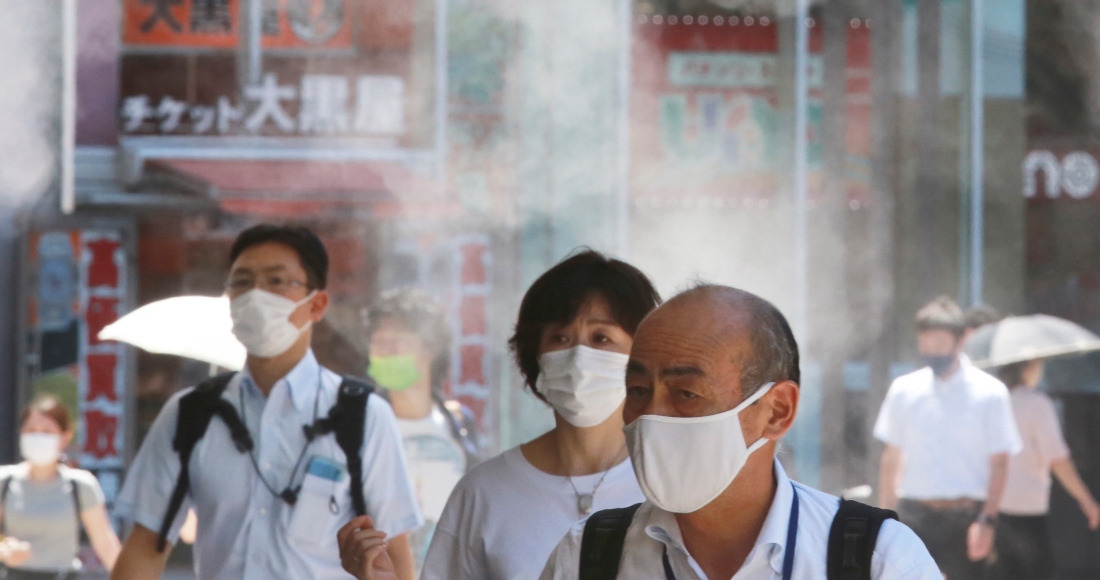 Gente con mascarillas para protegerse contra la expansión del coronavirus caminan bajo agua vaporizada en Tokio, el jueves 5 de agosto de 2021.