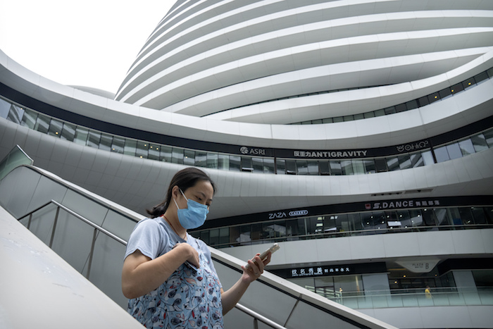 Una mujer con una mascarilla para protegerse del coronavirus camina en un complejo de tiendas y oficinas el martes 27 de julio de 2021, en Beijing.