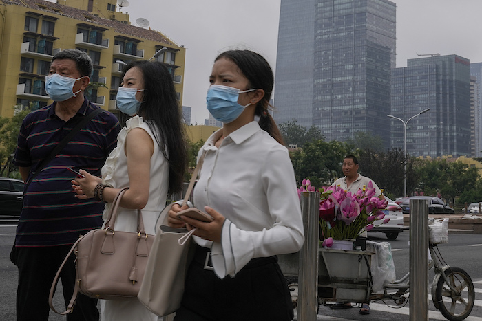 Varias personas con mascarillas para protegerse del coronavirus observan algo junto a un vendedor de flores afuera de una estación del tren subterráneo el jueves 22 de julio de 2021, en Beijing. 