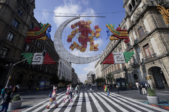 Varias personas pasan por debajo de una representación de Coyolxauhqui, la diosa precolombina de la luna, en la Plaza del Zócalo, en la Ciudad de México, el 9 de agosto de 2021.