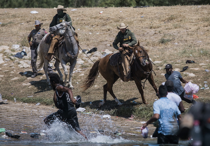 Agentes a caballo de la Oficina de Aduanas y Protección Fronteriza de Estados Unidos tratan de impedir que migrantes crucen el río Bravo desde Ciudad Acuña, México, a Del Río, Texas, el 19 de septiembre de 2021.