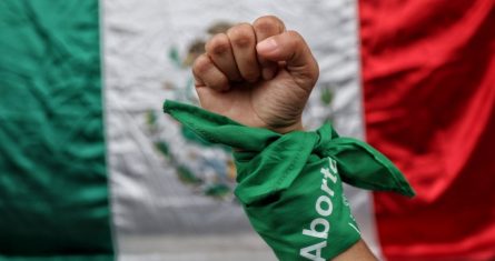 En la imagen una mujer posa con pañuelo verde símbolo del aborto legal, frente a una bandera de México durante el dictamen de la SCJN.