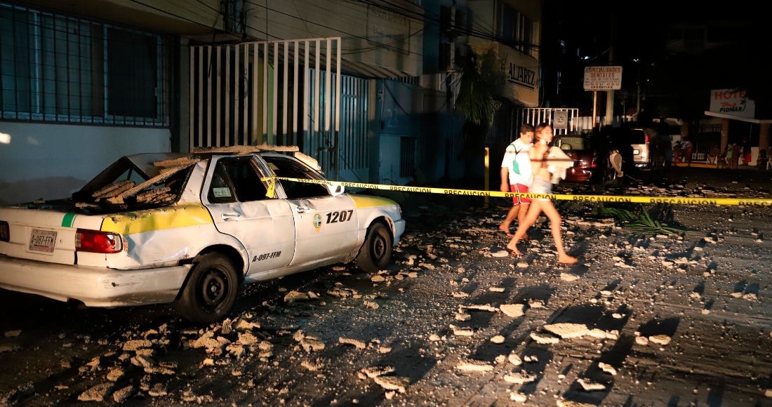 Unas personas pasan frente a un taxi dañado por la caída de escombros debido a un sismo en Acapulco, México, el 7 de septiembre de 2021.