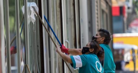 Un par de mujeres trabajan limpiando los cristales de un edificio en Paseo de la Reforma.