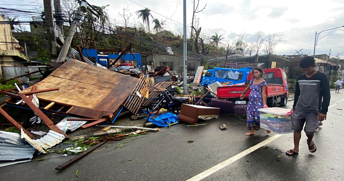 Residentes cargan con lo que queda de sus pertenencias mientras caminan frente a las casas dañadas por el tifón Rai en la ciudad de Surigao, en el centro de Filipinas, el viernes 17 de diciembre de 2021.