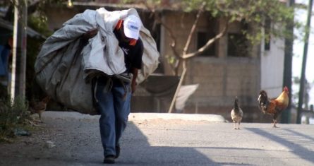 Un hombre camina por una calle del pueblo de Ocotepec, con una enorme bolsa de plástico donde va guardando las botellas de plástico o latas de aluminio que encuentra, las cuales venderá más tarde para allegarse de algunos pesos.