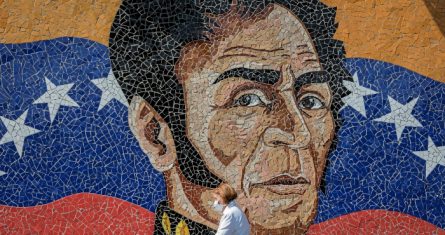 Una mujer con tapabocas y guantes camina frente a un mural del libertador Simón Bolívar en Caracas (Venezuela), en una fotografía de archivo.