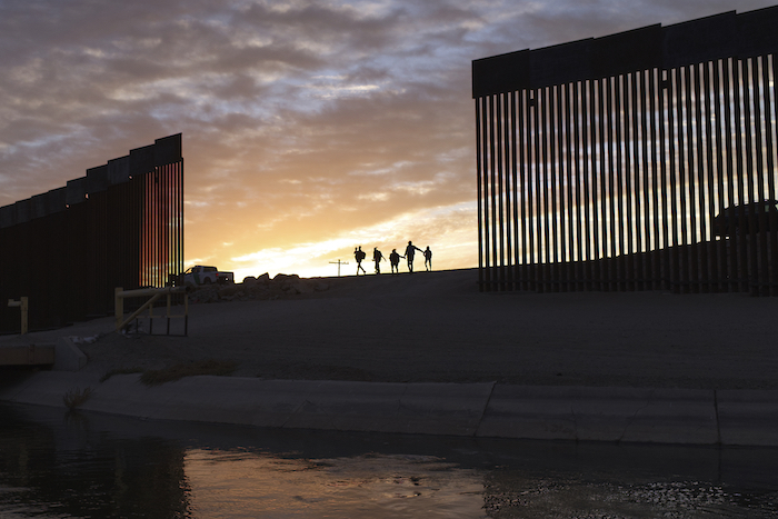 Dos familias migrantes de Brasil pasan por un hueco en la valla fronteriza para llegar a Estados Unidos tras cruzar desde México, en Yuma, Arizona, para pedir asilo el 10 de enero de 2021.