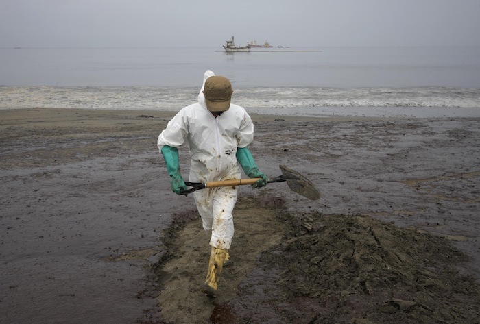 Un trabajador, vestido con un traje protector, limpia la playa Conchitas contaminada por un derrame de petróleo, en Ancón, Perú, el jueves 20 de enero de 2022.