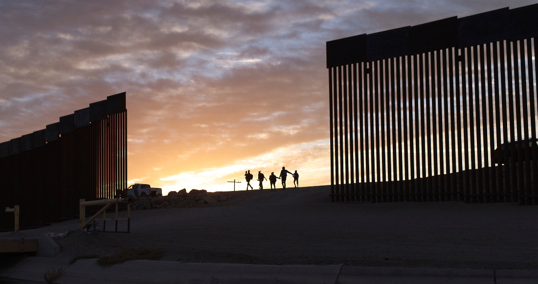 Dos familias migrantes de Brasil pasan por un hueco en la valla fronteriza para llegar a Estados Unidos tras cruzar desde México, en Yuma, Arizona, para pedir asilo el 10 de enero de 2021.