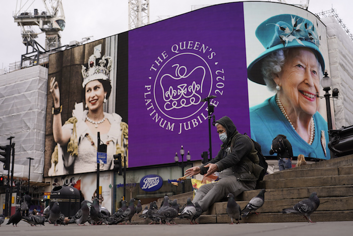 Un hombre alimenta a las palomas y a sus espaldas se ve una pantalla en Piccadilly Circus para celebrar el 70 aniversario del ascenso al trono de la reina Isabel de Gran Bretaña, en Londres, el domingo 6 de febrero de 2022.