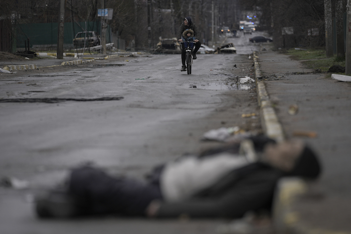 Un hombre y un niño van en bicicleta mientras los cuerpos de civiles yacen en la calle en el suburbio de Bucha, Ucrania, anteriormente ocupado por Rusia, en Kiev, el sábado 2 de abril de 2022.