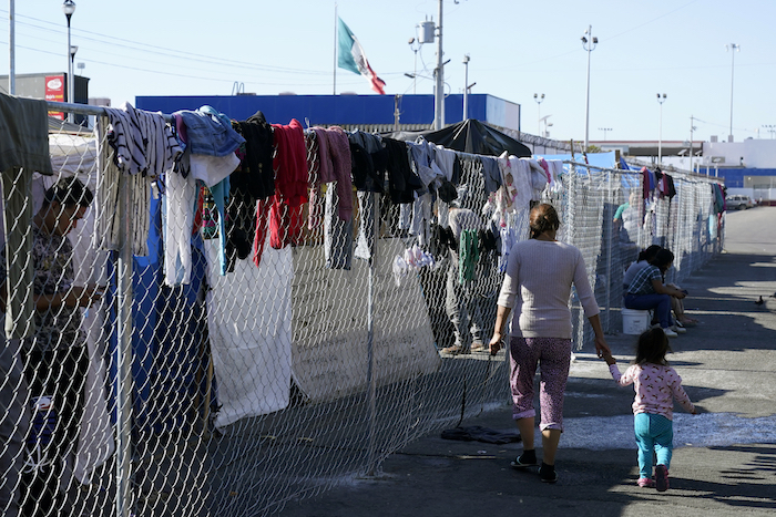 Una mujer migrante y su hija caminan junto a una cerca de un campamento improvisado en un cruce peatonal, donde residen cientos de migrantes que esperan solicitar asilo en Estados Unidos, el 8 de noviembre de 2021, en Tijuana, México.